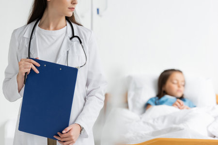 Pediatrician holding clipboard near blurred patient in hospital wardの写真素材