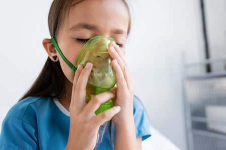 Ill child in patient gown using oxygen mask in clinicの写真素材