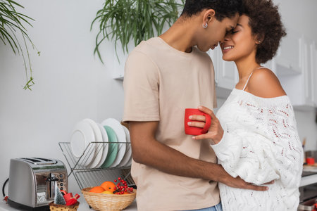happy african american couple embracing in kitchen near toaster and wicker basket with fresh orangesの写真素材