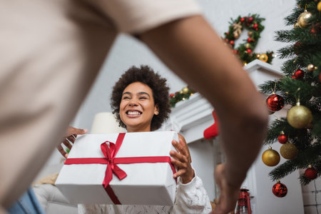 low angle view of overjoyed african american woman holding large gift box near christmas tree and blurred boyfriendの写真素材