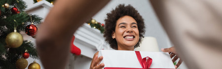 low angle view of laughing african american woman with christmas present near blurred boyfriend, bannerの写真素材