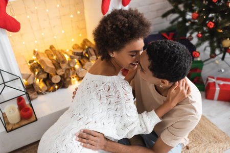 sexy african american woman in white openwork sweater embracing with man near fireplaceの写真素材