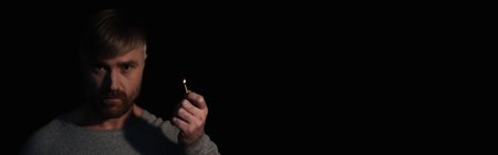 man looking at camera while holding lit match during power outage isolated on black, bannerの写真素材