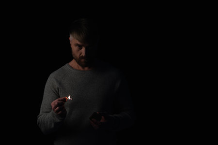 displeased man holding burning match during energy blackout isolated on blackの写真素材