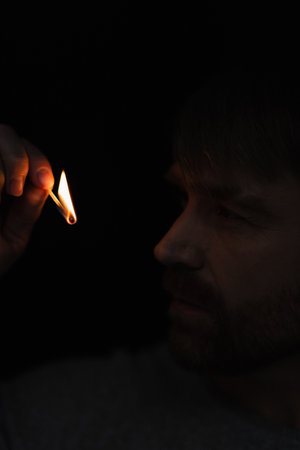 man looking at flame of burning match in darkness isolated on black