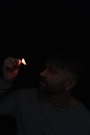 man looking at flame of burning match during power outage isolated on blackの写真素材