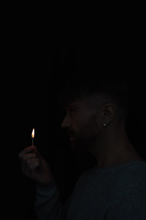 side view of man holding burning match during energy blackout isolated on blackの写真素材