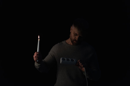 man with lit candle looking at  socket extender during power outage isolated on blackの写真素材
