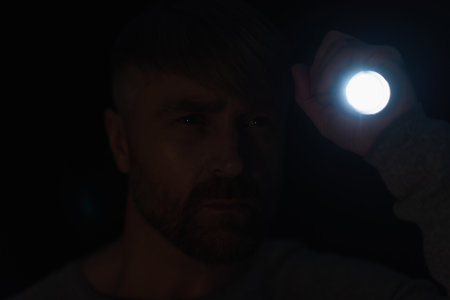 man lighting with flashlight at camera during power outage isolated on blackの写真素材
