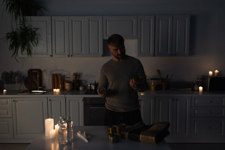 man holding canned food near table with bottled water and candlesの写真素材