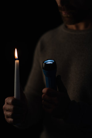 cropped view of man with flashlight and burning candle isolated on black
