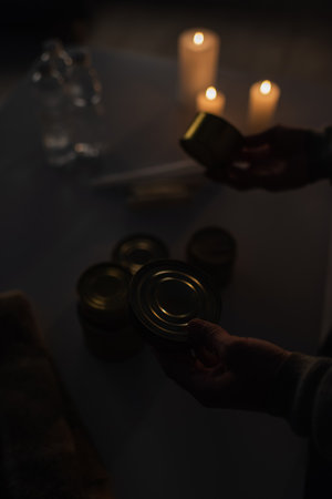 cropped view of man near reserve of canned food and candles burning on blurred background