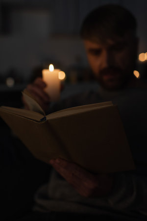 selective focus of book near man holding lit candle while reading during electricity shutdownの写真素材