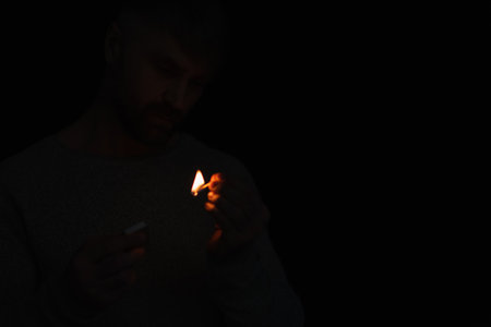man with matchbox looking at burning match during energy blackout isolated on black