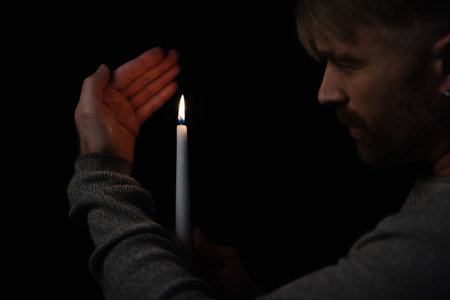 man looking at flame of burning candle during power outage isolated on blackの写真素材