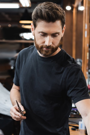 bearded brunette barber holding scissors in beauty salon