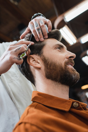 low angle view of hairstylist cutting hair of bearded smiling manの写真素材