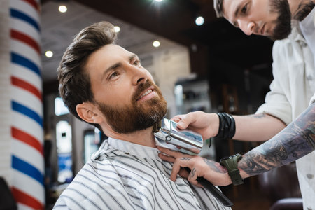bearded man smiling while barber shaving his neck with electric razorの写真素材