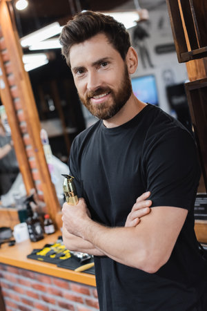 happy hairstylist holding hair clipper while smiling at camera in barbershopの写真素材
