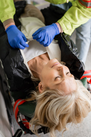 Paramedic taking off clothes from unconscious mature woman in emergency vehicle