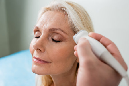blonde woman with closed eyes near doctor doing ultrasound examination of her head