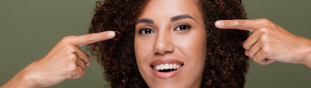 Positive african american woman pointing at eyes and looking at camera isolated on green, banner