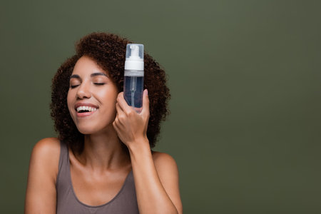 Pleased african american woman holding cleansing foam isolated on greenの写真素材