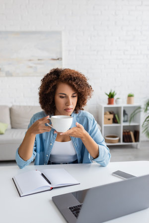 African american freelancer holding cup near gadgets and notebook on tableの写真素材