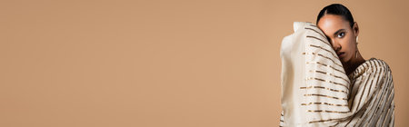 elegant african american woman in golden earring looking at camera while posing isolated on beige,...