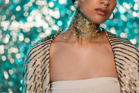 cropped view of african american woman with piercing and gold on neck posing on sparkling blue backgroundの写真素材