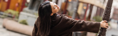 back view of brunette woman in coat posing near lamppost on street in prague, banner
