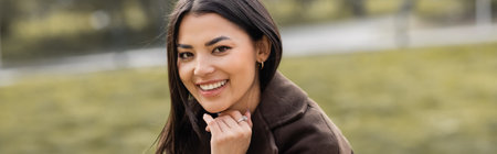 Smiling brunette woman in coat looking at camera outdoors, banner
