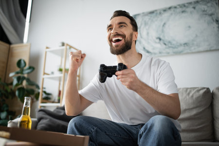 excited man playing video game near pizza and bottle of beer at homeの写真素材