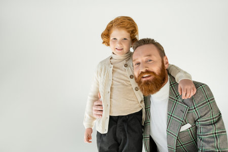 Smiling bearded father hugging redhead son isolated on greyの写真素材
