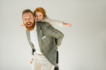 Excited bearded father playing with son isolated on greyの写真素材