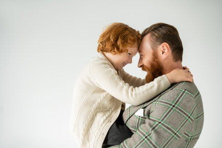 Side view of smiling red haired child embracing stylish dad isolated on greyの写真素材