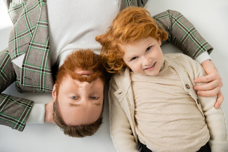 top view of redhead dad and son in stylish clothing lying on grey backgroundの写真素材