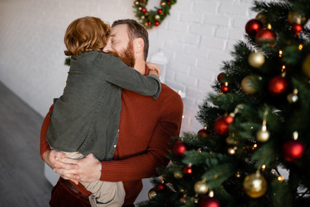 redhead boy hugging dad holding him near decorated Christmas treeの写真素材