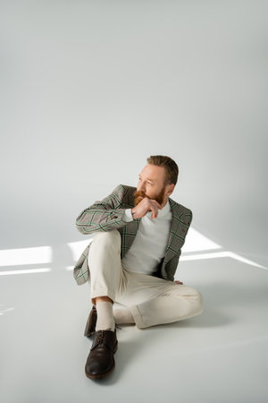 Bearded man in plaid jacket looking away while sitting on grey background with sunlightの写真素材