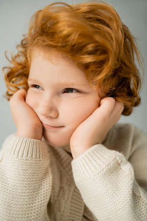 Portrait of red haired kid in beige knitted jumper looking away isolated on greyの写真素材