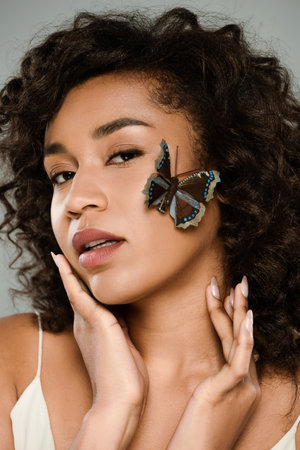 pretty african american woman with butterfly on face isolated on grey