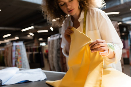 curly salesperson holding yellow fabric while working in textile shopの写真素材