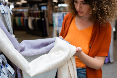Blurred curly customer holding textured cloth in textile shopの写真素材