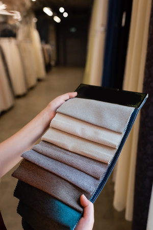Cropped view of young woman holding cloth samples in blurred textile shop