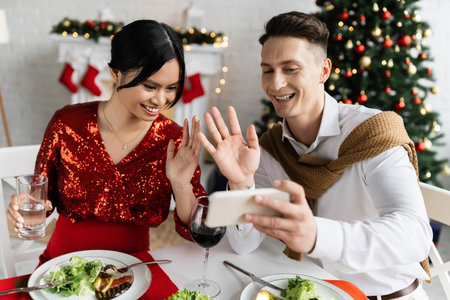 pregnant asian woman with smiling husband waving hands during video call on smartphone at Christmas celebrationの写真素材