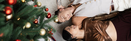 top view of happy interracial couple lying under Christmas tree, banner