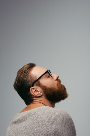 Side view of trendy bearded man in eyeglasses closing eye isolated on greyの写真素材