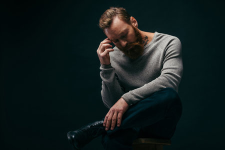 Fashionable bearded and tattooed man posing while sitting on chair isolated on blackの写真素材