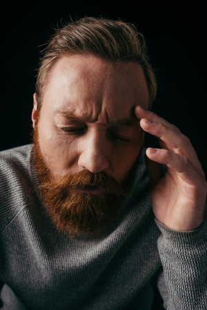Portrait of worried man in long sleeve touching forehead isolated on blackの写真素材