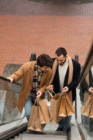 high angle view of stylish and happy gay men looking into shopping bags on escalatorの写真素材